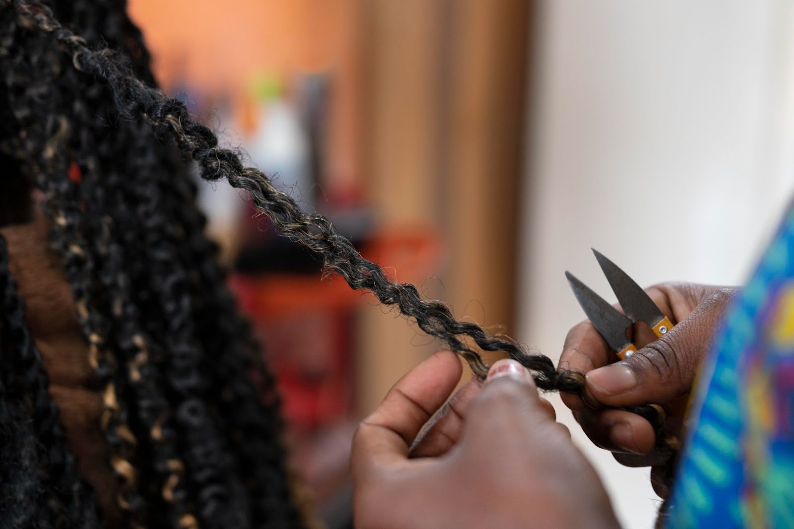 How To Braid African Hair: A Guide for New Cosmetologists 1 Close-up of hands cutting a strand of twisted hair with scissors in a hair salon.