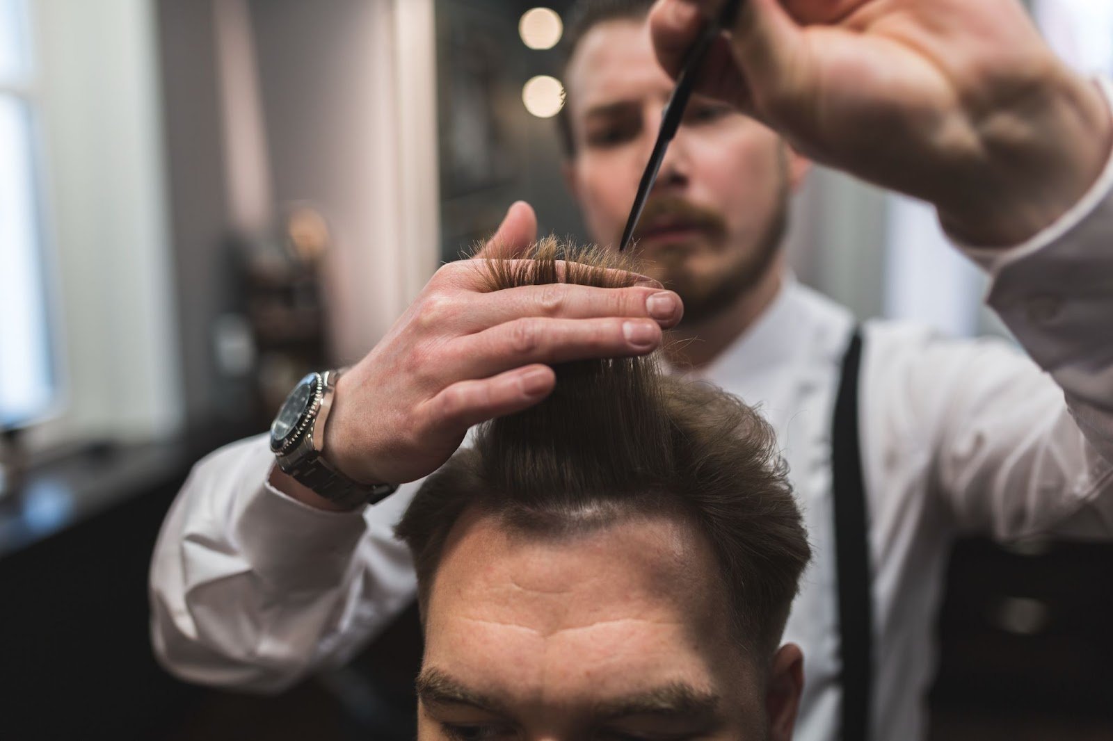 Top Tips on Cutting Men’s Hair: A Guide for Beginners & Future Barbers 4 Barber styling a client’s hair with a comb and scissors in a professional barbershop