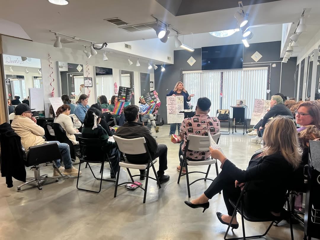 How to Choose a Beauty School: Making The Right Decision 3 Classroom setting in a beauty school, with students seated in a circle listening to an instructor at the front of the room holding up a color chart.