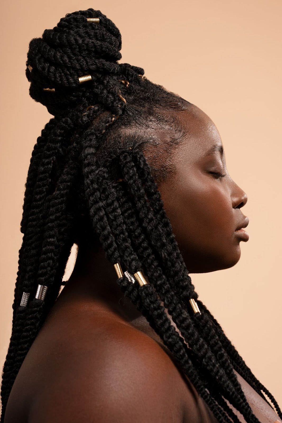 How To Braid African Hair: A Guide for New Cosmetologists 8 Side profile of a woman with jumbo Senegalese twists styled in a high bun with gold hair cuffs.