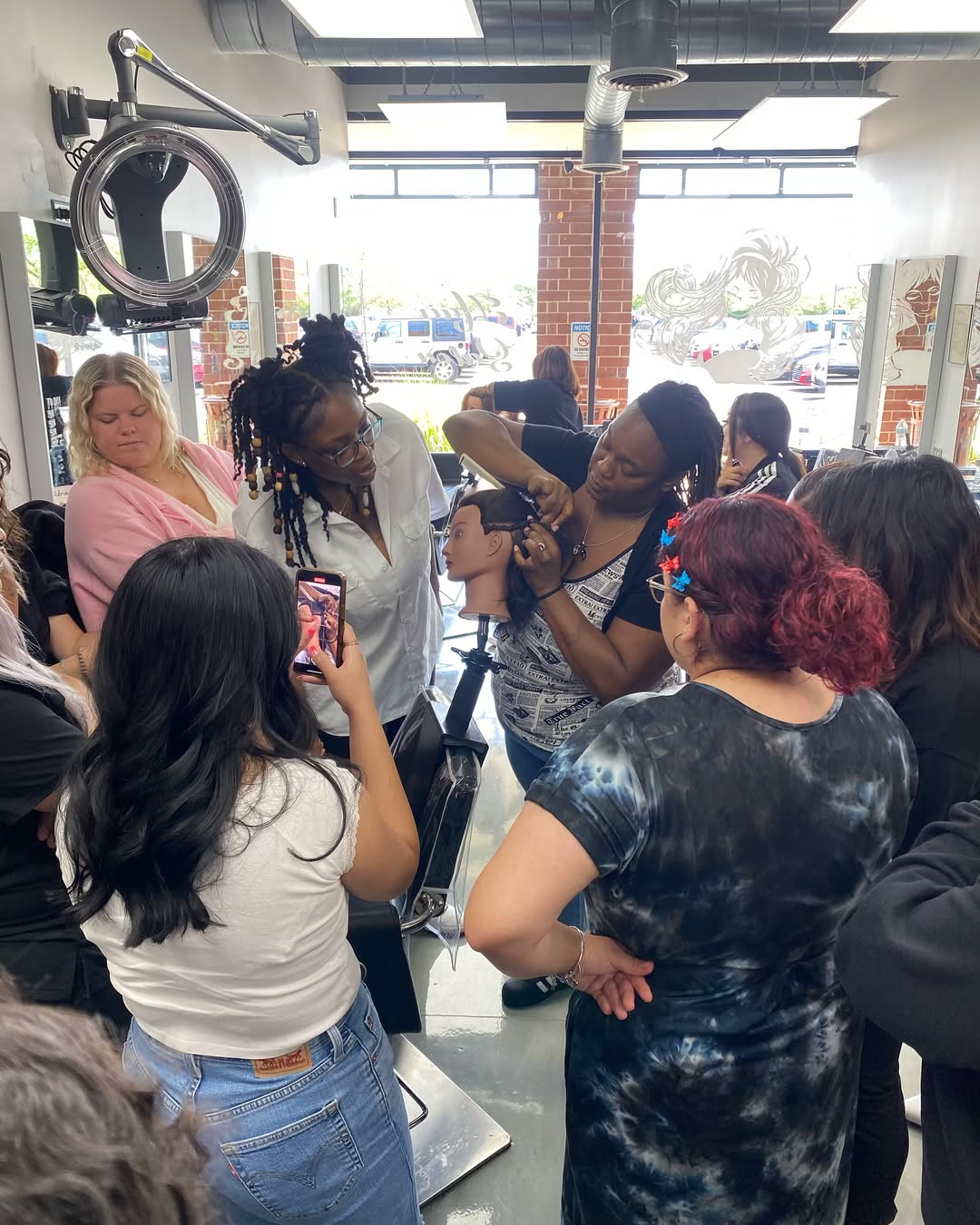 How To Braid African Hair: A Guide for New Cosmetologists 9 Group of cosmetology students watching a live braiding demonstration on a mannequin head in a classroom.