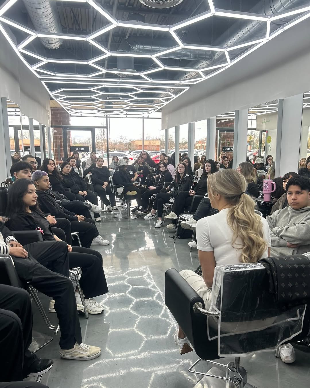 How to Choose a Beauty School: Making The Right Decision 4 Beauty school students attentively listening to an instructor in a modern classroom with geometric ceiling lights.