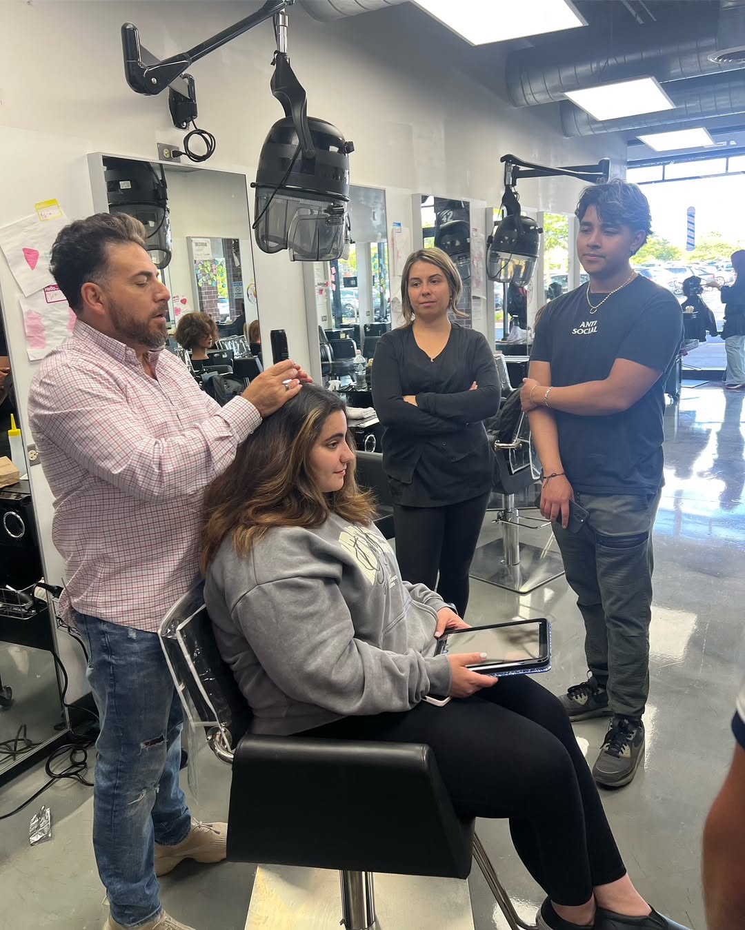 Cosmetology instructor showing students how to section hair on a seated client during hands-on salon training.