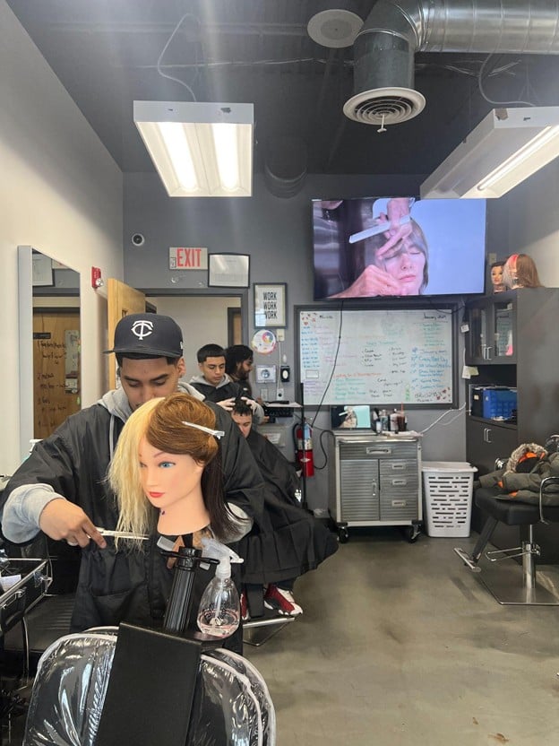 Cosmetology student practicing haircutting techniques on a mannequin during cosmetology classes at Cosmetology & Spa Academy.
