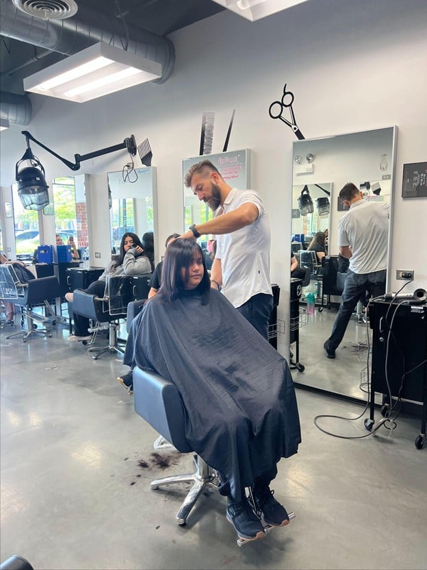 Cosmetology student providing a supervised haircut to a client on the salon floor at Cosmetology & Spa Academy beauty school in Illinois.