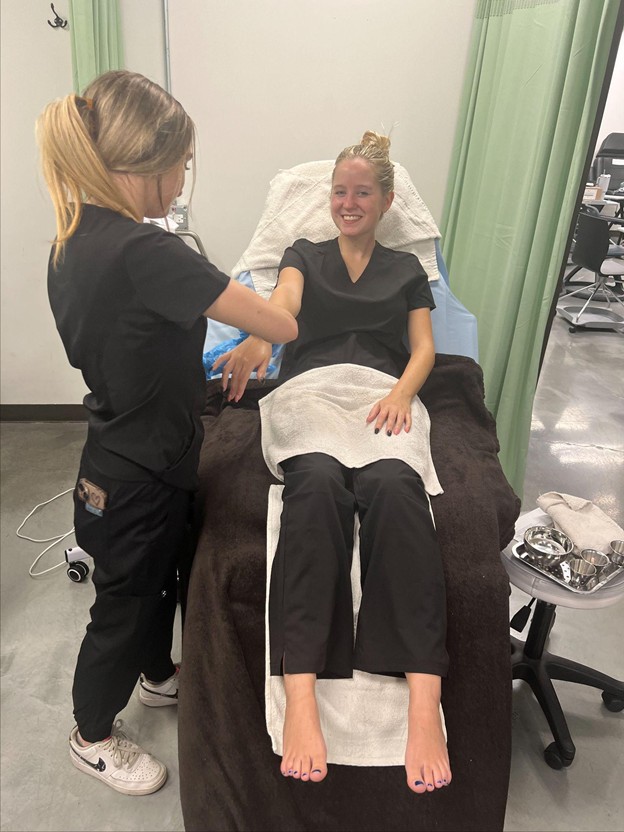 Esthetics student providing supervised hair removal treatment to a client in the student clinic at Cosmetology & Spa Academy in Illinois.