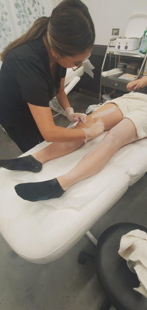 Esthetics student performing professional leg waxing during hands-on training at Cosmetology & Spa Academy, an esthetics school in Illinois.