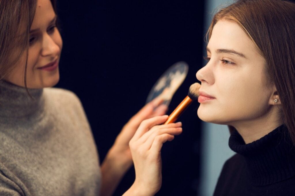 Makeup artist applying face powder to a model during professional makeup training at Cosmetology & Spa Academy, an Illinois beauty school.