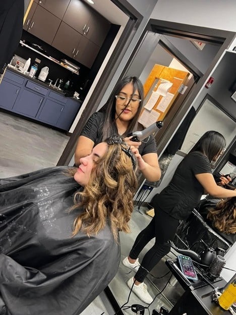 Cosmetology student performing professional hairstyling in a salon for a cosmetology portfolio example.