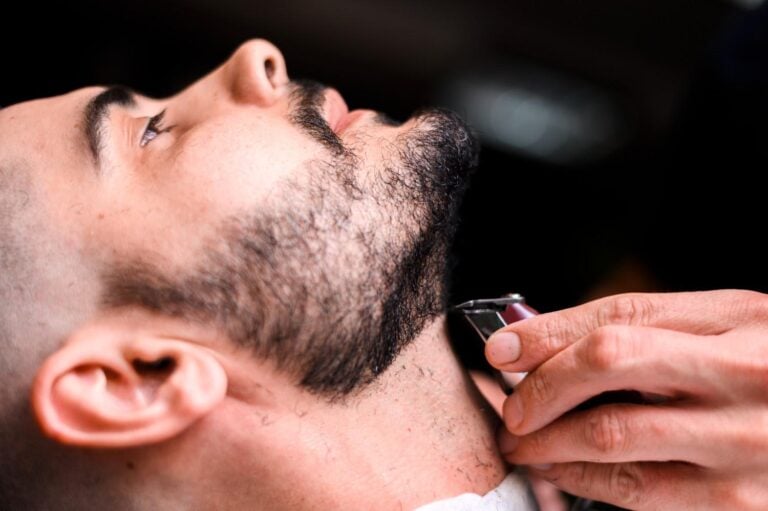 Close-up of barber carefully trimming a client’s beard line with electric trimmer.